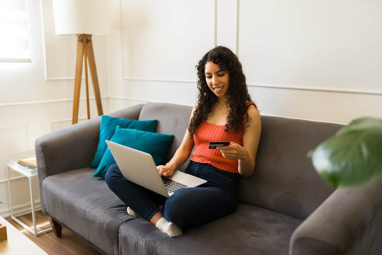 Woman holding a credit card while shopping online on a laptop at home.